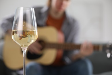Photo of Glass with white wine and man playing guitar indoors, selective focus