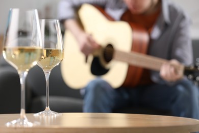 Photo of Glasses with white wine on table and man playing guitar indoors, selective focus