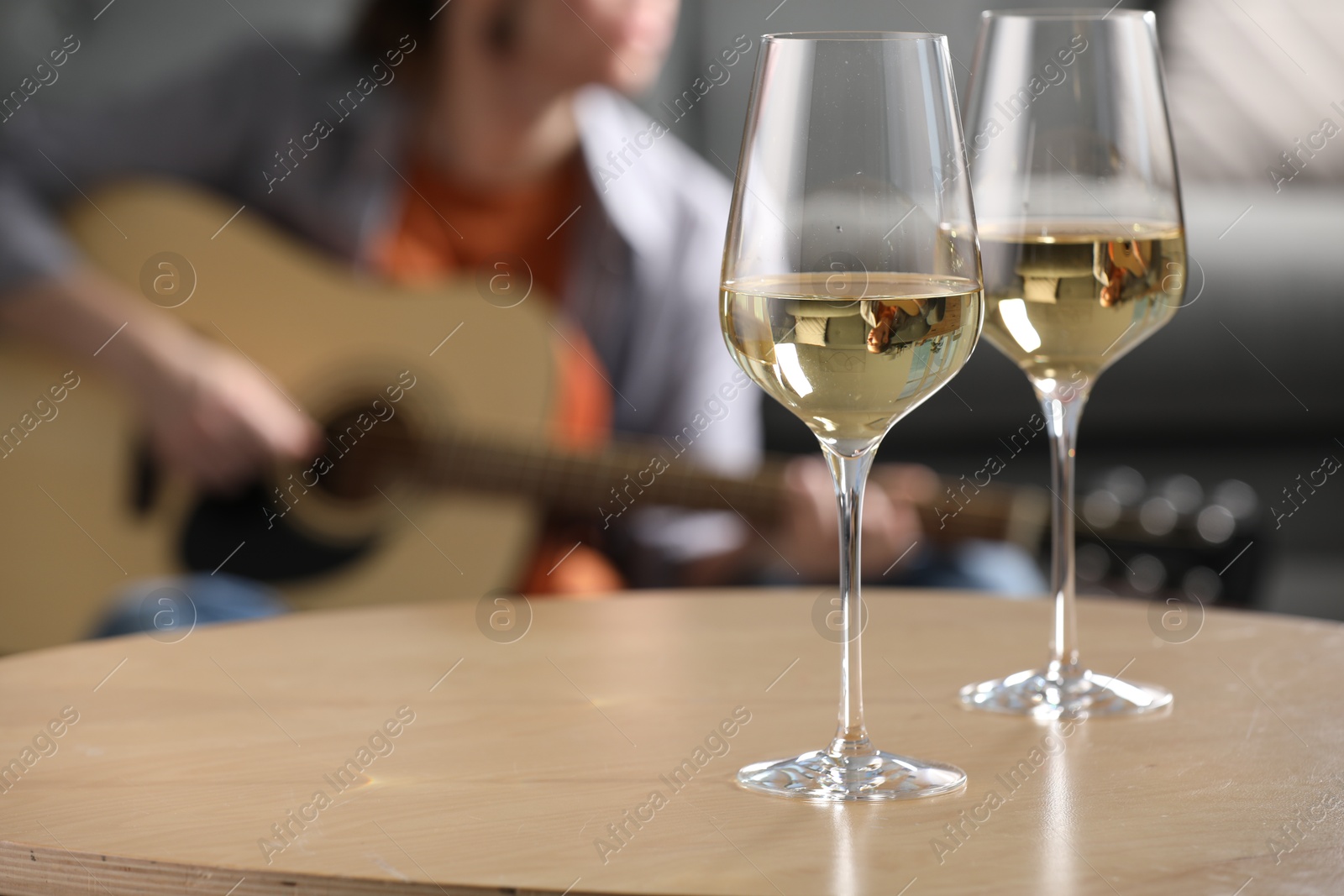 Glasses with white wine on table and man playing guitar indoors, selective focus Photo of Glasses with white wine on table and man playing guitar indoors, selective focus