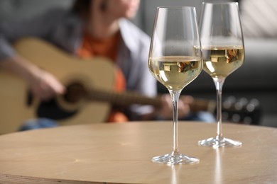 Photo of Glasses with white wine on table and man playing guitar indoors, selective focus