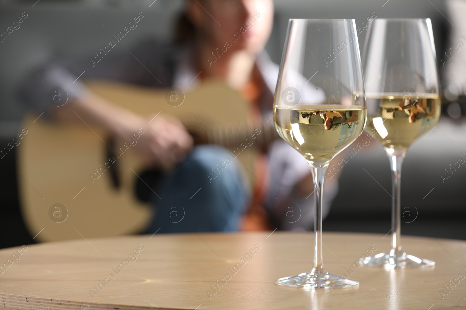 Glasses with white wine on table and man playing guitar indoors, selective focus Photo of Glasses with white wine on table and man playing guitar indoors, selective focus