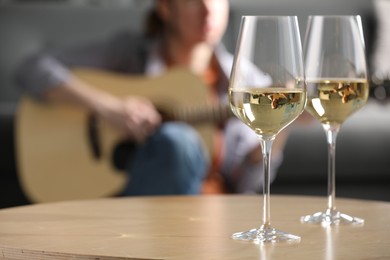 Photo of Glasses with white wine on table and man playing guitar indoors, selective focus