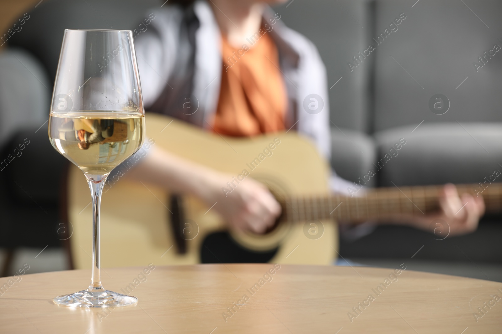 Glass with white wine on table and man playing guitar indoors, selective focus Photo of Glass with white wine on table and man playing guitar indoors, selective focus
