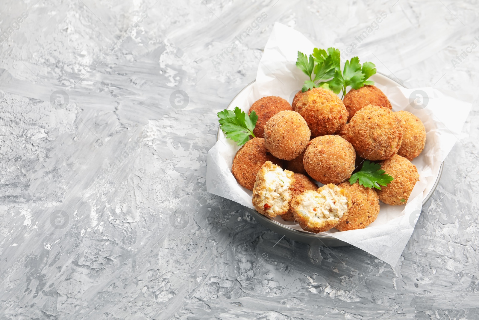 Photo of Delicious fried croquette balls with parsley in bowl on grey textured table. Space for text