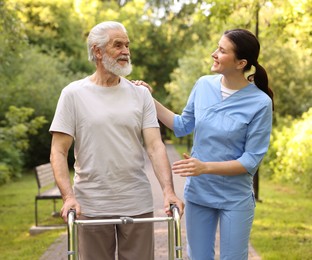 Photo of Smiling nurse supporting elderly man who using walking frame outdoors