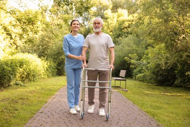 Photo of Smiling nurse supporting elderly man who using walking frame outdoors