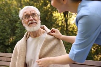 Photo of Nurse supporting smiling elderly man in glasses outdoors, closeup