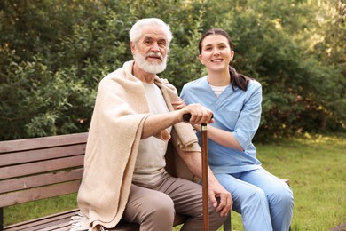 Photo of Smiling nurse with elderly man on bench outdoors