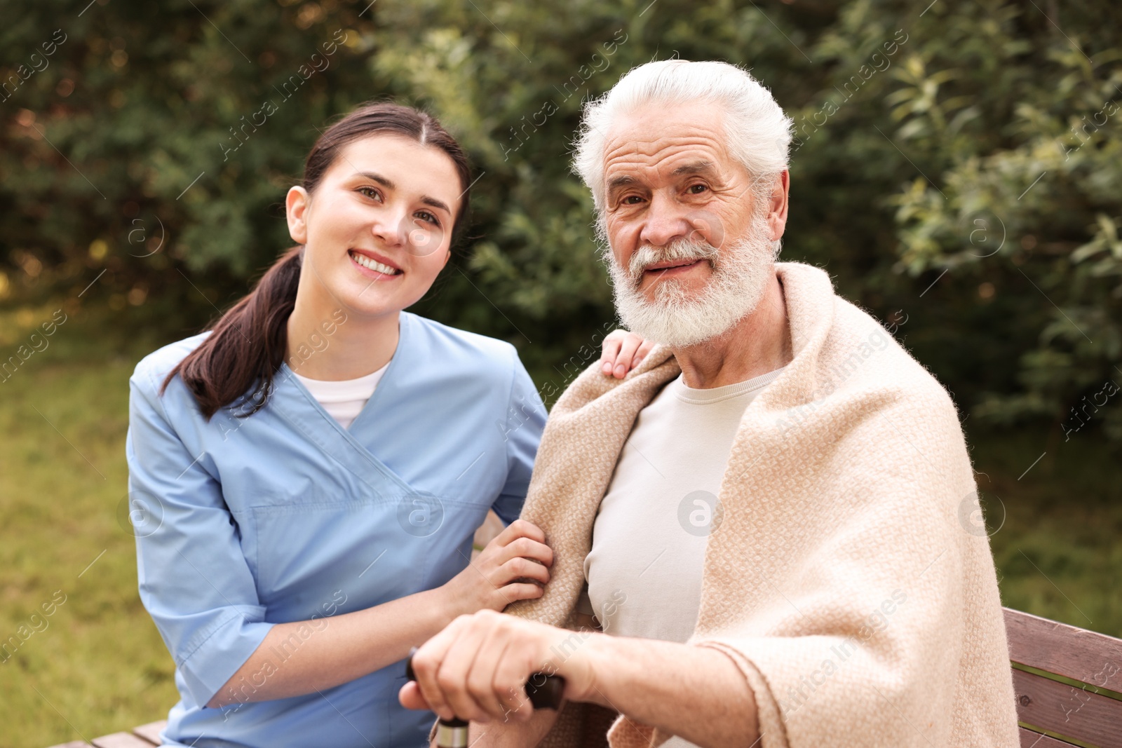 Smiling nurse with elderly man on bench outdoors Photo of Smiling nurse with elderly man on bench outdoors