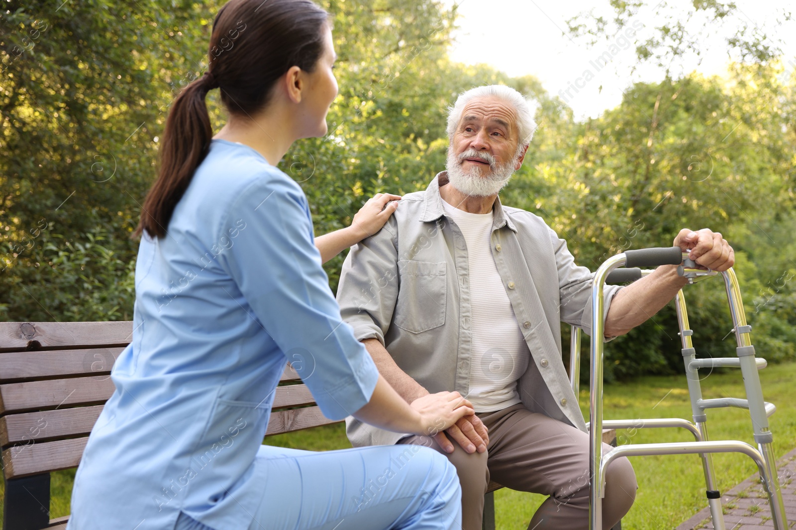 Nurse supporting elderly man with walking frame on bench outdoors Photo of Nurse supporting elderly man with walking frame on bench outdoors