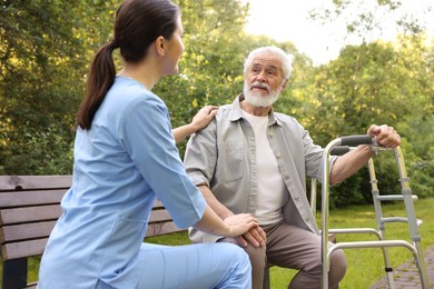 Photo of Nurse supporting elderly man with walking frame on bench outdoors