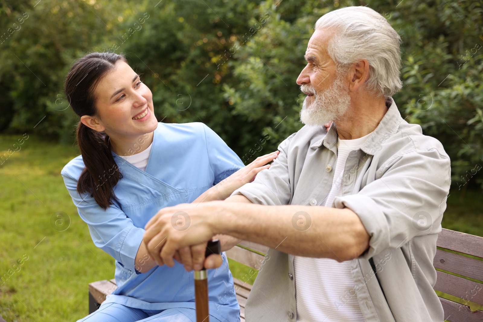 Smiling nurse supporting elderly man with walking cane on bench outdoors Photo of Smiling nurse supporting elderly man with walking cane on bench outdoors