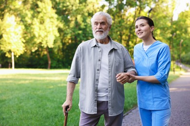 Photo of Smiling nurse supporting elderly man with walking cane outdoors