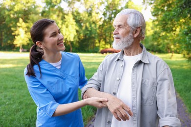 Photo of Smiling nurse supporting elderly man with walking cane outdoors