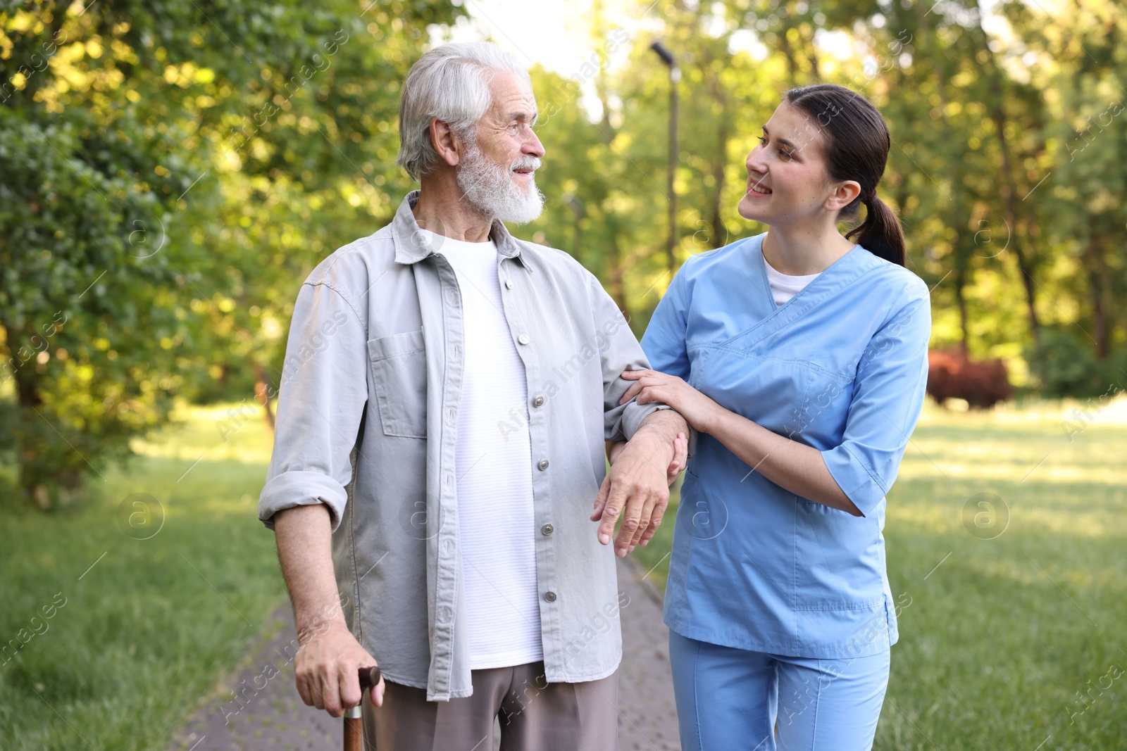 Smiling nurse supporting elderly man with walking cane outdoors Photo of Smiling nurse supporting elderly man with walking cane outdoors