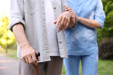 Photo of Nurse supporting elderly man with walking cane outdoors, closeup