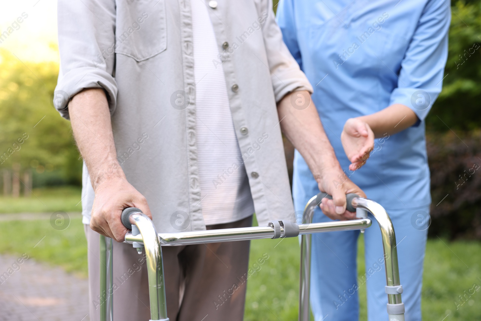 Nurse helping elderly man who using walking frame outdoors, closeup Photo of Nurse helping elderly man who using walking frame outdoors, closeup