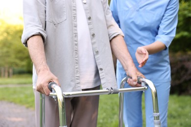 Photo of Nurse helping elderly man who using walking frame outdoors, closeup