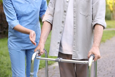 Photo of Nurse helping elderly man who using walking frame outdoors, closeup