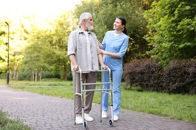 Photo of Smiling nurse supporting elderly man who using walking frame outdoors