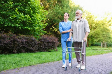 Photo of Smiling nurse with elderly man who using walking frame outdoors. Space for text