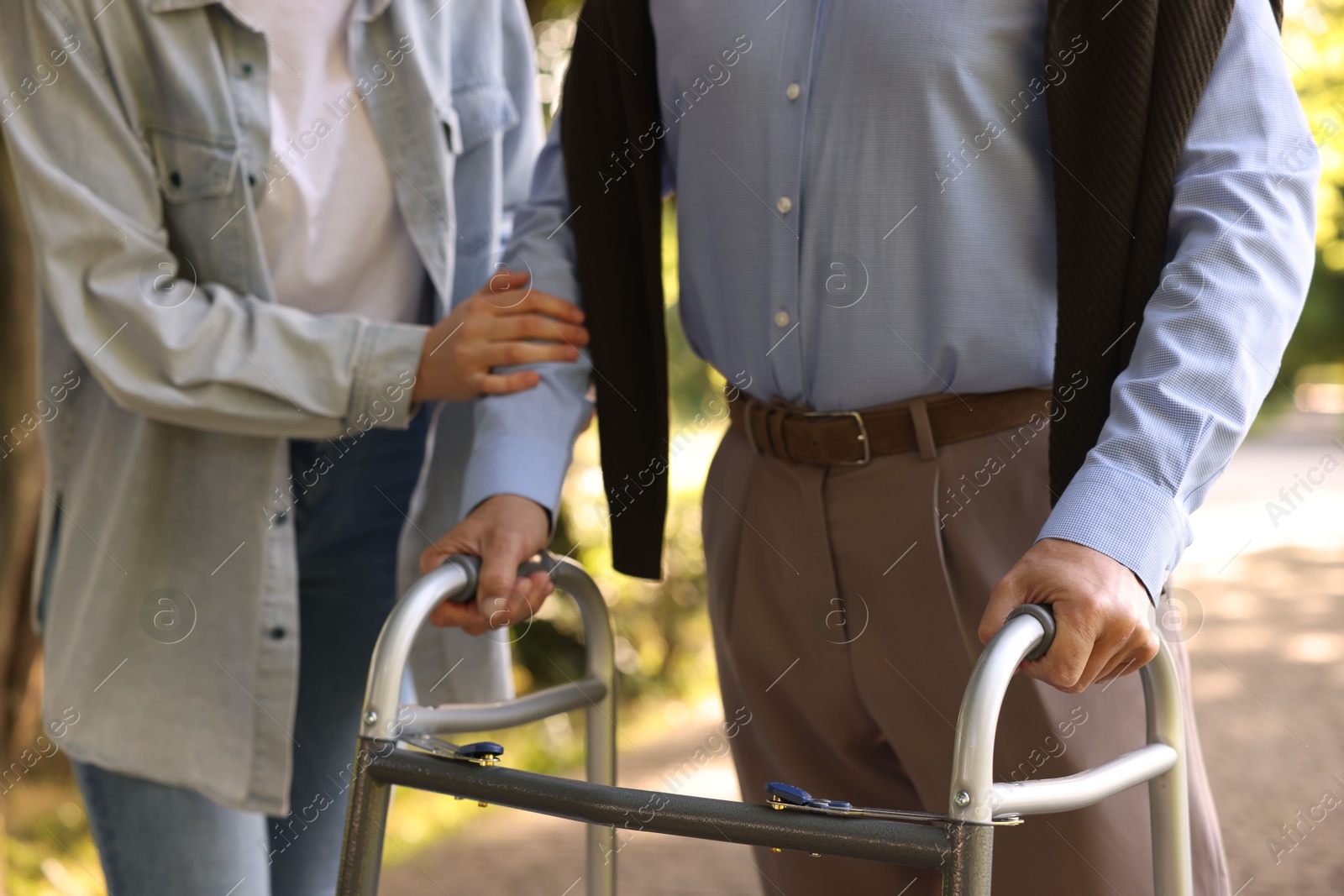 Caregiver supporting elderly man who using walking frame outdoors, closeup Photo of Caregiver supporting elderly man who using walking frame outdoors, closeup