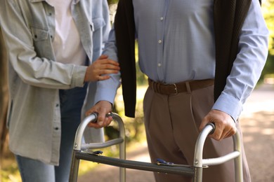 Photo of Caregiver supporting elderly man who using walking frame outdoors, closeup