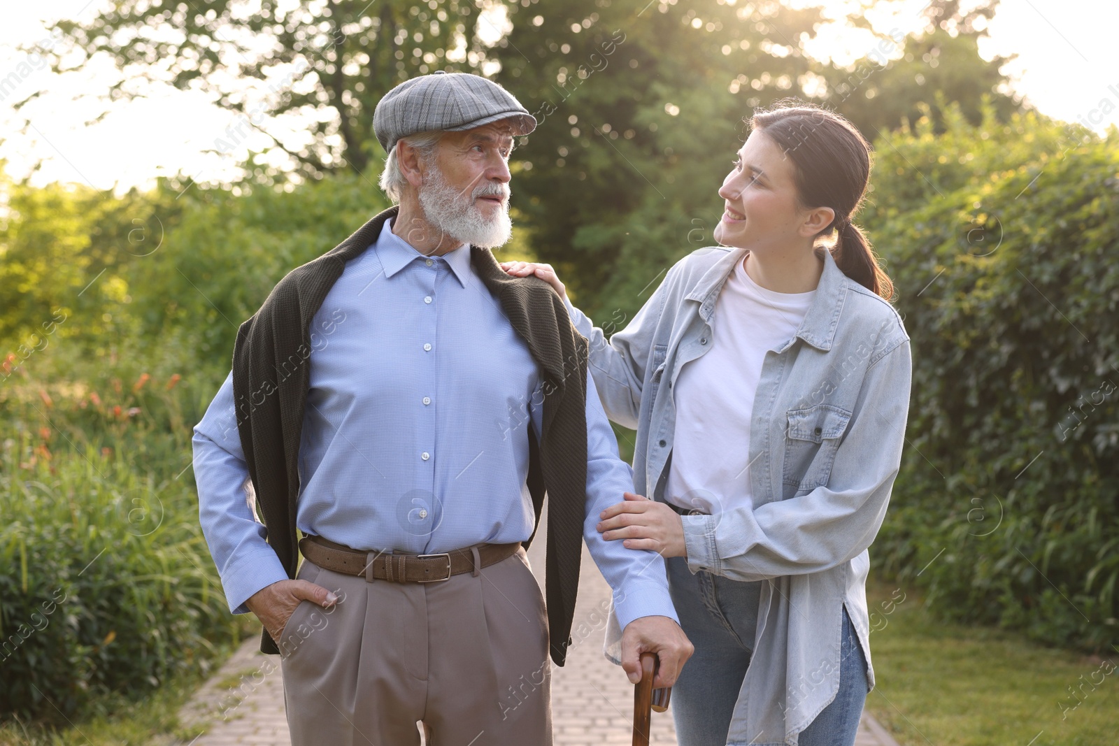 Smiling caregiver supporting elderly man with walking cane outdoors Photo of Smiling caregiver supporting elderly man with walking cane outdoors