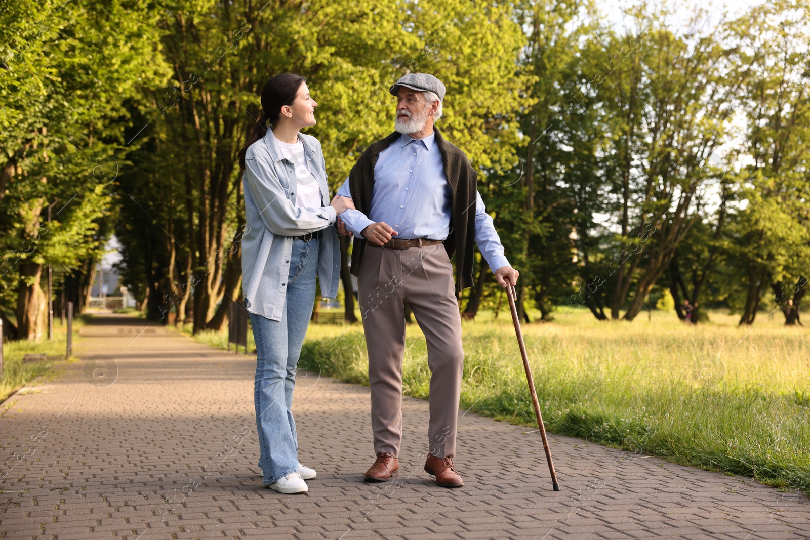 Smiling caregiver supporting elderly man with walking cane outdoors Photo of Smiling caregiver supporting elderly man with walking cane outdoors
