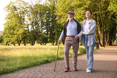 Photo of Smiling caregiver supporting elderly man with walking cane outdoors. Space for text