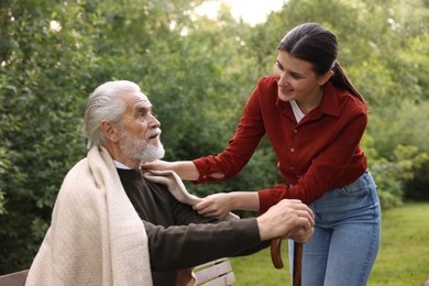 Photo of Smiling caregiver supporting elderly man with walking cane outdoors