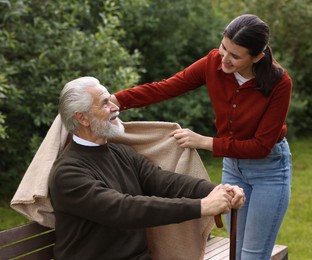 Photo of Smiling caregiver helping elderly man with walking cane outdoors