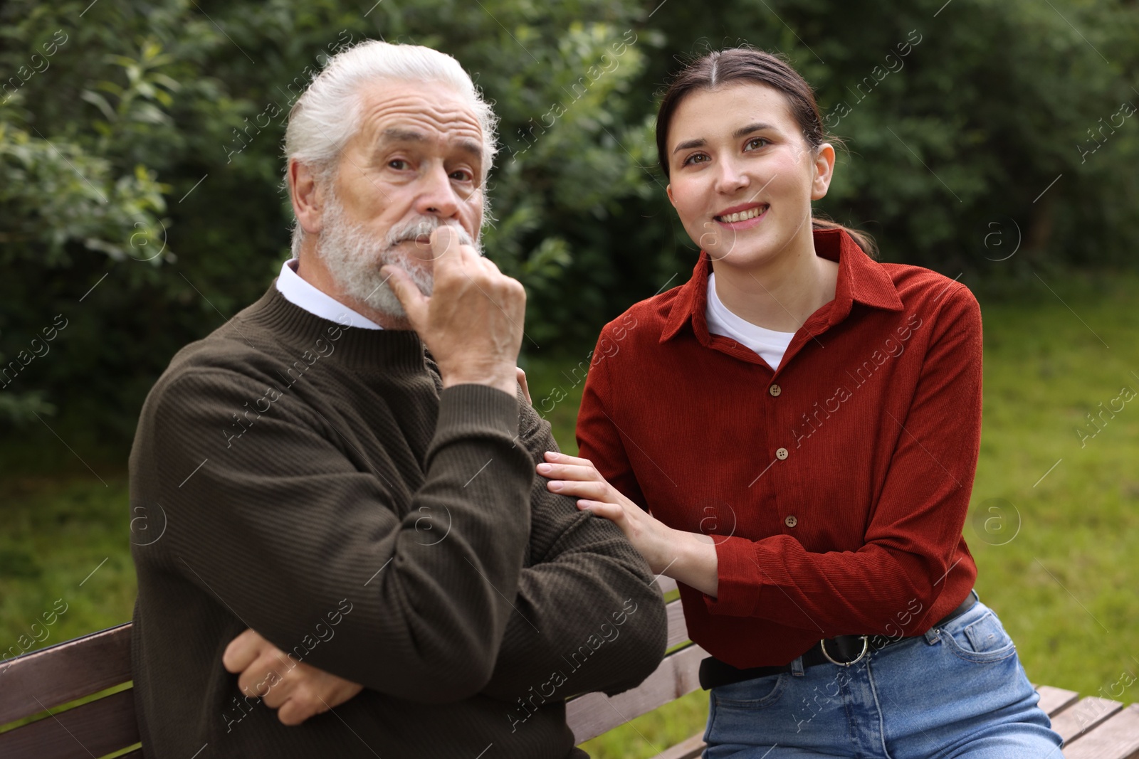 Portrait of smiling caregiver with elderly man on bench outdoors Photo of Portrait of smiling caregiver with elderly man on bench outdoors