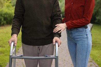 Photo of Caregiver supporting elderly man who using walking frame outdoors, closeup