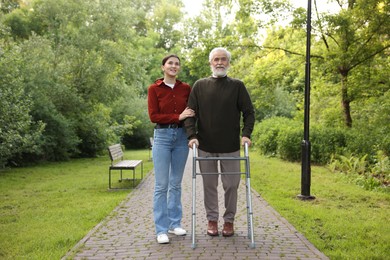 Photo of Smiling caregiver supporting elderly man who using walking frame outdoors