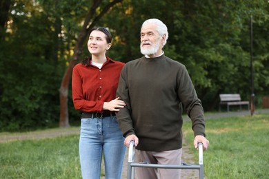 Photo of Smiling caregiver supporting elderly man who using walking frame outdoors