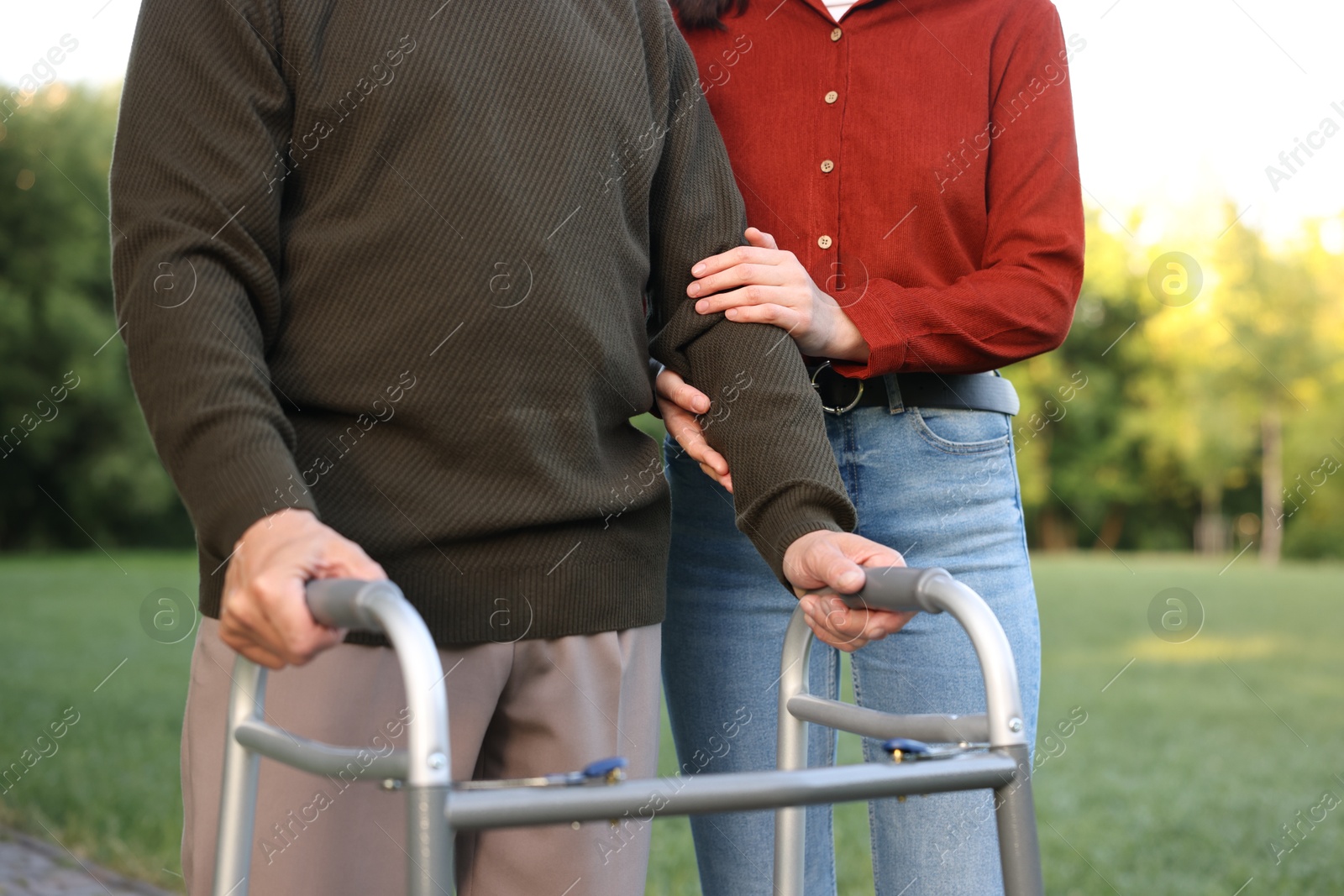 Caregiver supporting elderly man who using walking frame outdoors, closeup Photo of Caregiver supporting elderly man who using walking frame outdoors, closeup