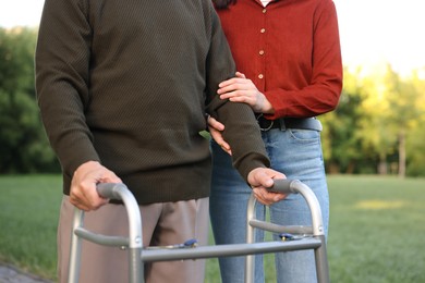 Photo of Caregiver supporting elderly man who using walking frame outdoors, closeup