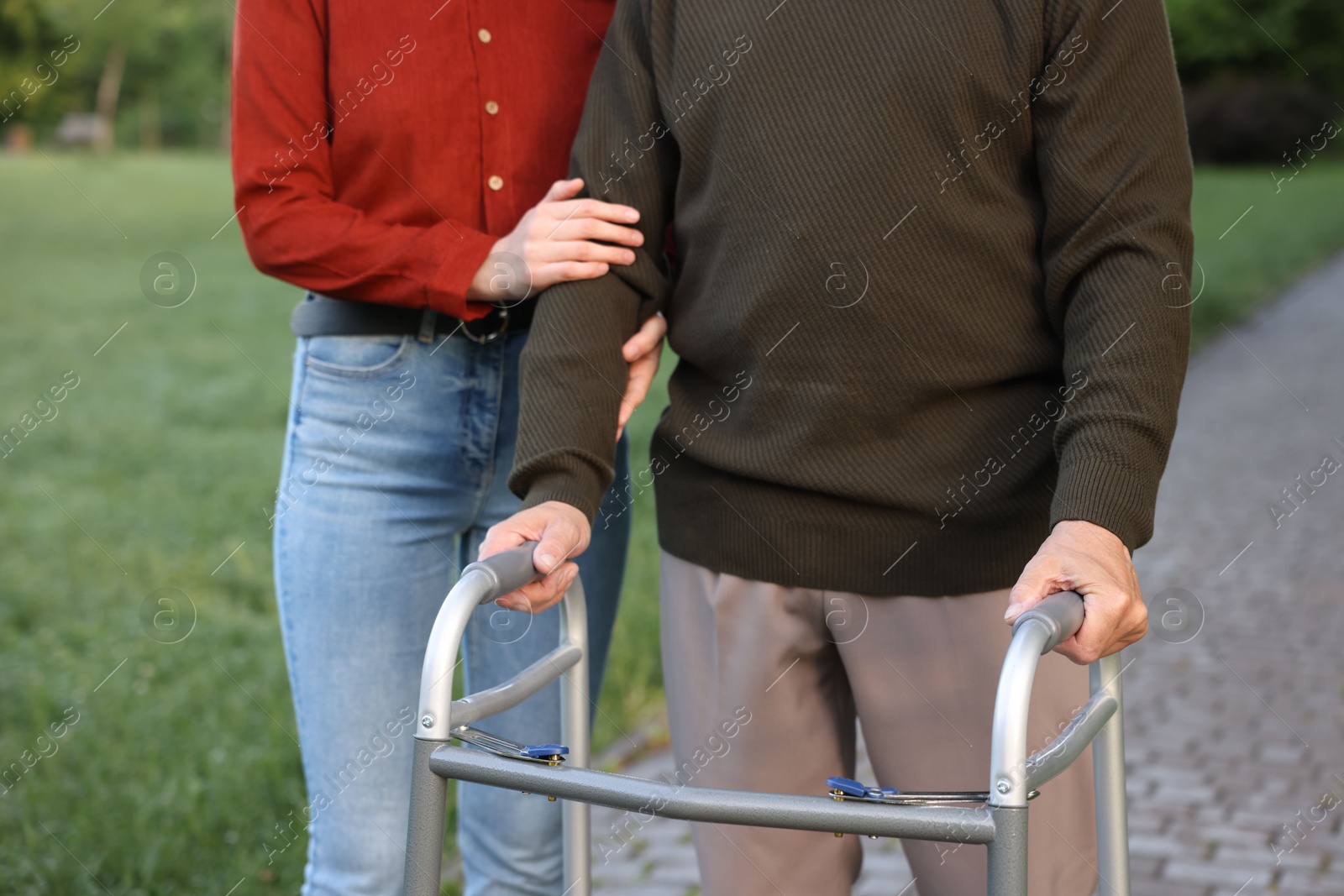 Caregiver supporting elderly man who using walking frame outdoors, closeup Photo of Caregiver supporting elderly man who using walking frame outdoors, closeup