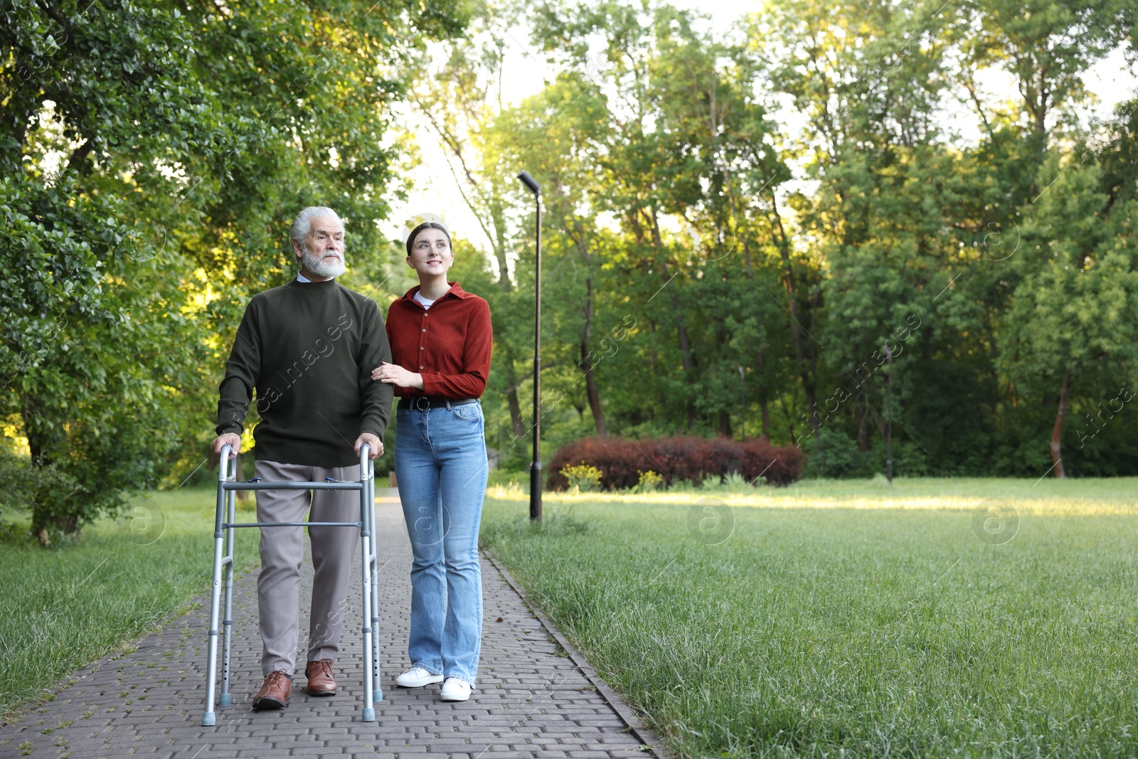 Smiling caregiver supporting elderly man who using walking frame outdoors. Space for text Photo of Smiling caregiver supporting elderly man who using walking frame outdoors. Space for text
