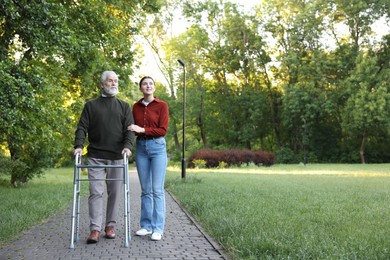 Photo of Smiling caregiver supporting elderly man who using walking frame outdoors. Space for text