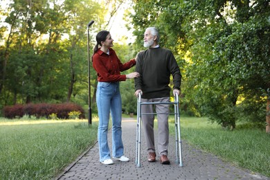 Photo of Smiling caregiver supporting elderly man who using walking frame outdoors