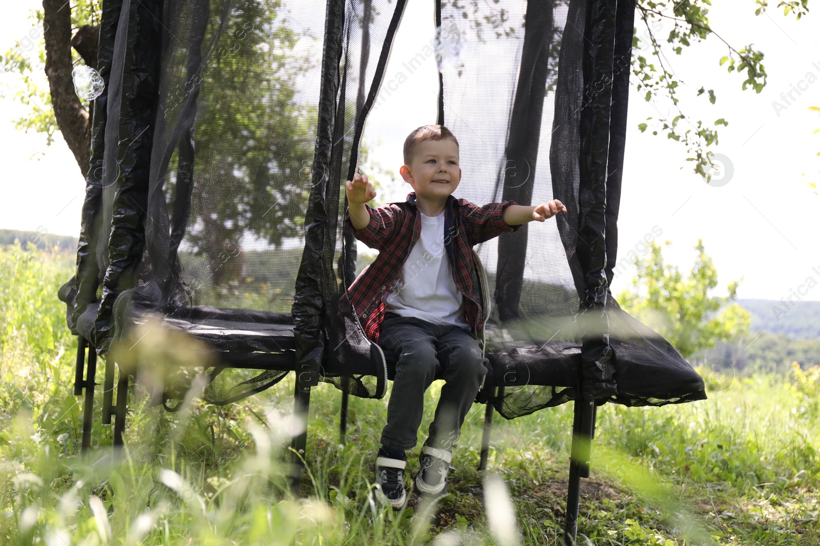 Happy boy sitting on black trampoline outdoors Photo of Happy boy sitting on black trampoline outdoors