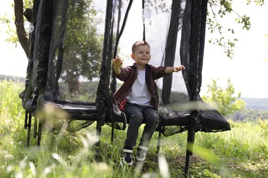 Photo of Happy boy sitting on black trampoline outdoors