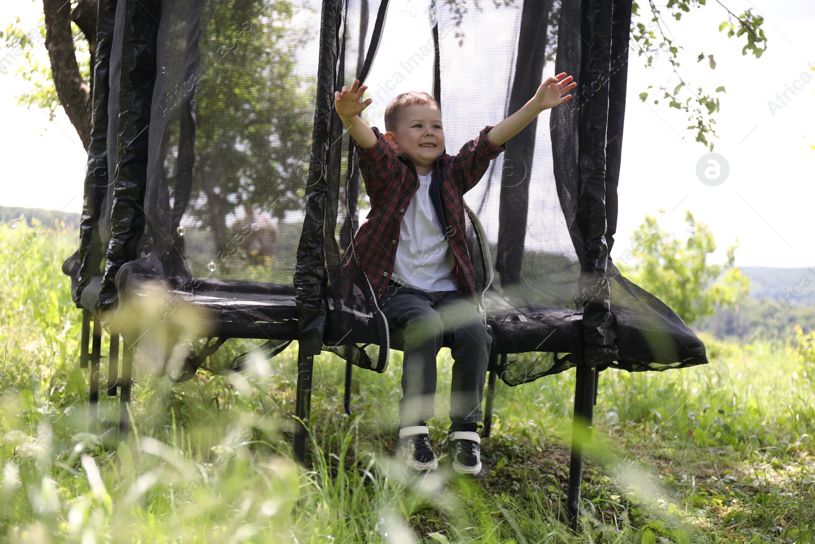 Photo of Happy boy sitting on black trampoline outdoors
