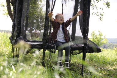 Photo of Happy boy sitting on black trampoline outdoors