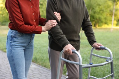 Photo of Caregiver supporting elderly man who using walking frame outdoors, closeup