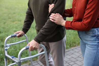 Photo of Caregiver supporting elderly man who using walking frame outdoors, closeup