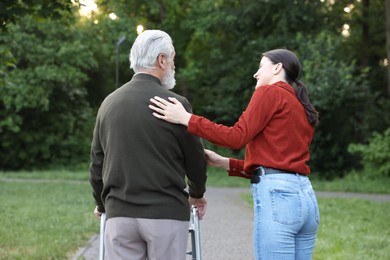 Photo of Caregiver supporting elderly man who using walking frame outdoors, back view