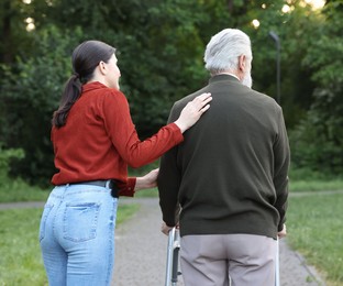 Photo of Caregiver supporting elderly man who using walking frame outdoors, back view